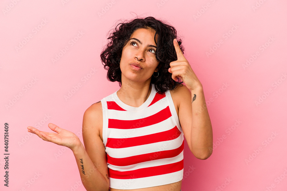 Young curly latin woman isolated on pink background holding and showing a product on hand. Young curly latin woman isolated on pink background holding and showing a product on hand.