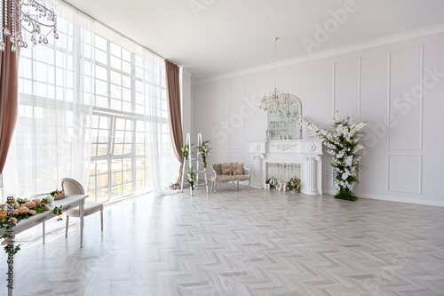 luxurious bright spacious guest room with beautiful chic furniture a huge floor-to-ceiling window in a royal style is decorated with green plants, white walls with stucco and a fireplace © 4595886