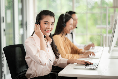 Team of call center staff in Asia wears headphones with a microphone. Smile while serving customers at desks and computers. Service concept and consulting. Communication concept.