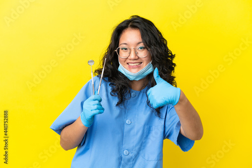 Young asian dentist holding tools over isolated background with thumbs up because something good has happened