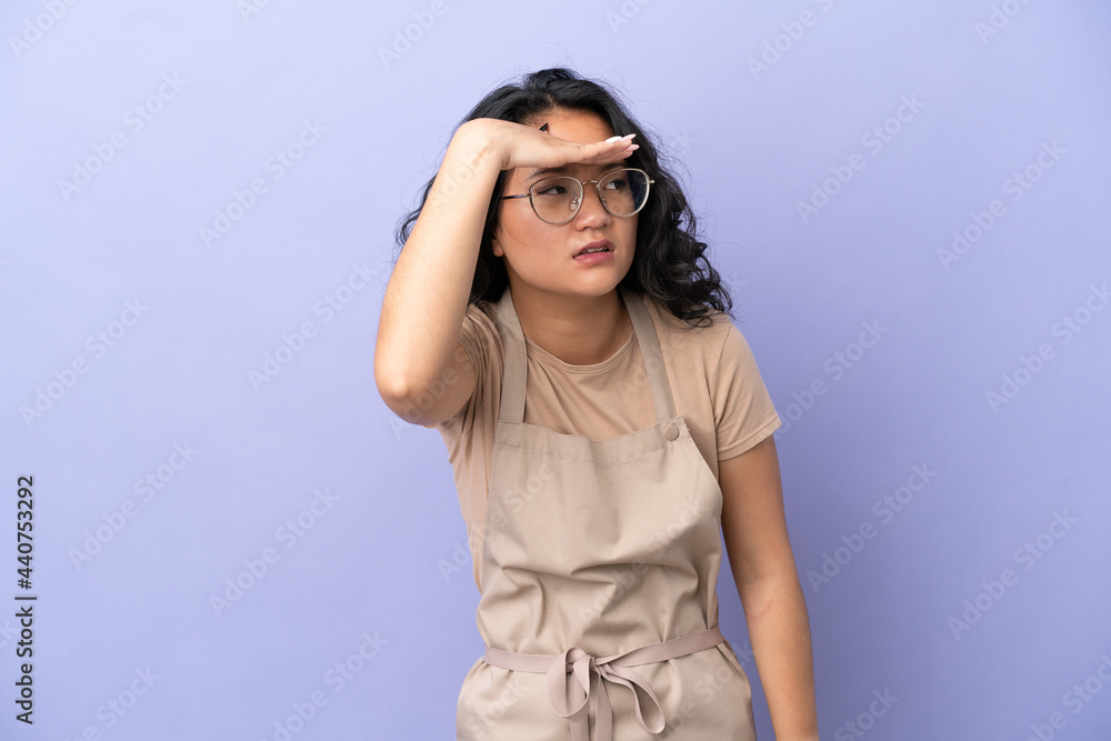 Restaurant asian waiter isolated on purple background looking far away with hand to look something Restaurant asian waiter isolated on purple background looking far away with hand to look something