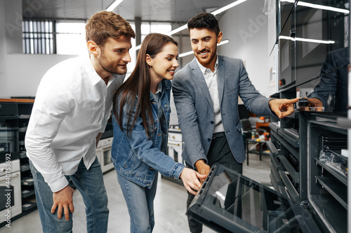 Male shop assistant helps young couple to choose new home appliance