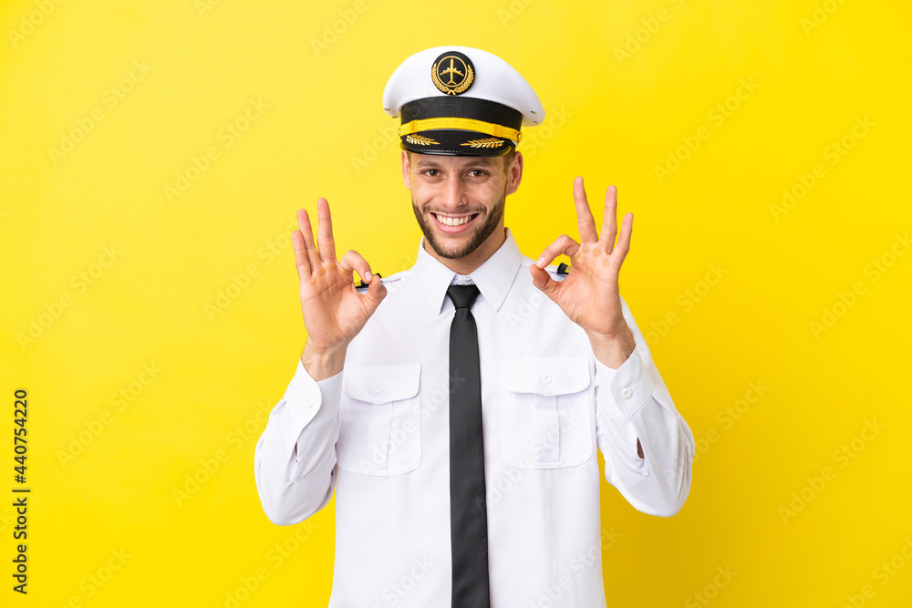 Airplane caucasian pilot isolated on yellow background showing an ok sign with fingers Airplane caucasian pilot isolated on yellow background showing an ok sign with fingers