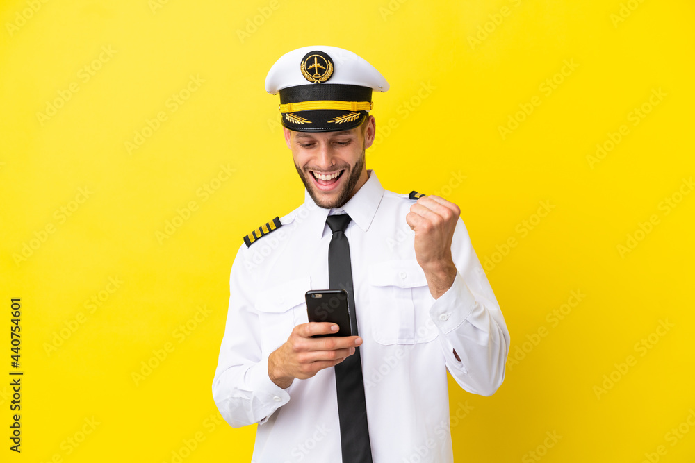 Airplane caucasian pilot isolated on yellow background with phone in victory position