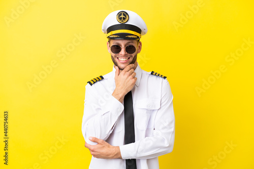 Airplane caucasian pilot isolated on yellow background with glasses and smiling © luismolinero
