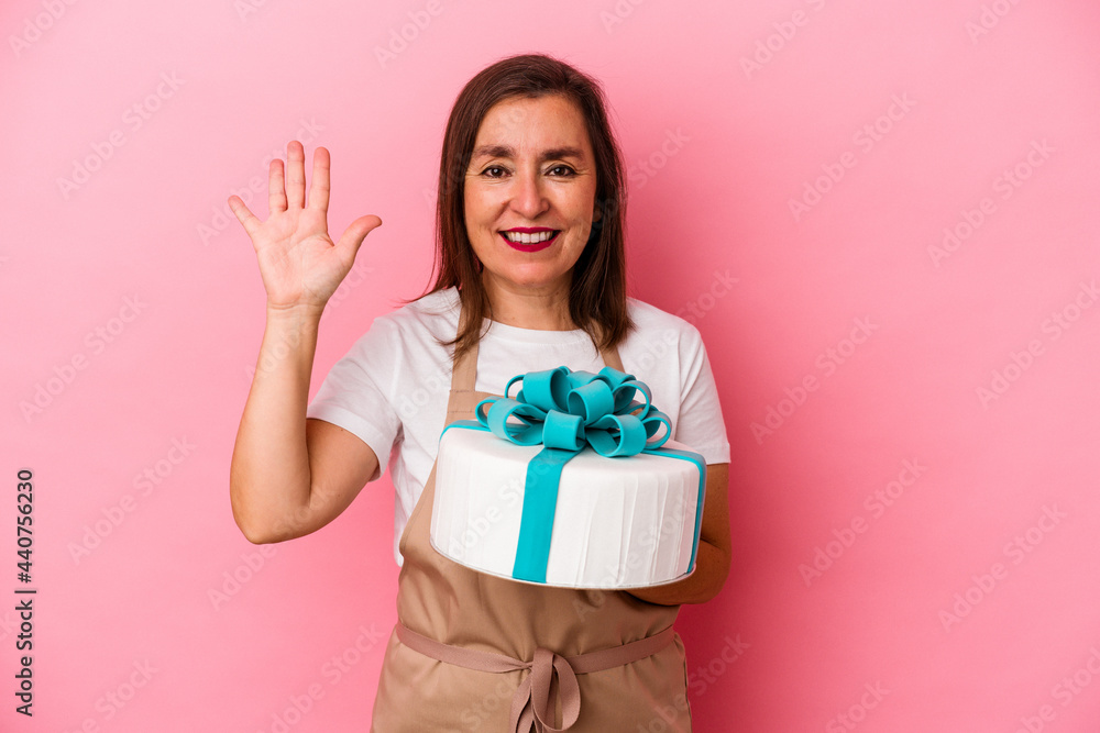 Middle aged pastry chef woman holding a cake isolated on blue background smiling cheerful showing number five with fingers. Middle aged pastry chef woman holding a cake isolated on blue background smiling cheerful showing number five with fingers.