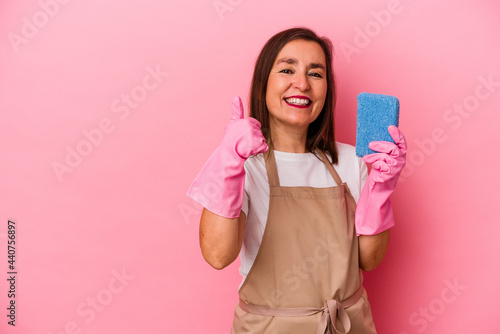 Middle age caucasian woman cleaning home isolated on pink background smiling and raising thumb up