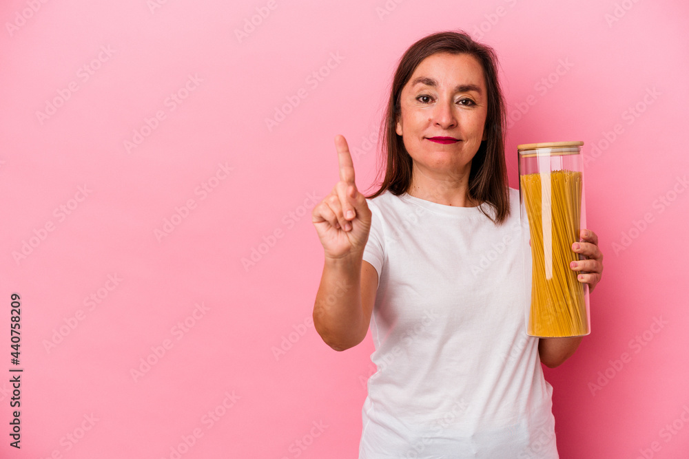Middle age caucasian woman holding a pasta jar isolated on pink background showing number one with finger. Middle age caucasian woman holding a pasta jar isolated on pink background showing number one with finger.