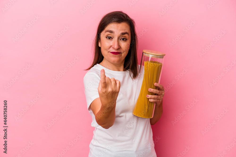 Middle age caucasian woman holding a pasta jar isolated on pink background pointing with finger at you as if inviting come closer. Middle age caucasian woman holding a pasta jar isolated on pink background pointing with finger at you as if inviting come closer.