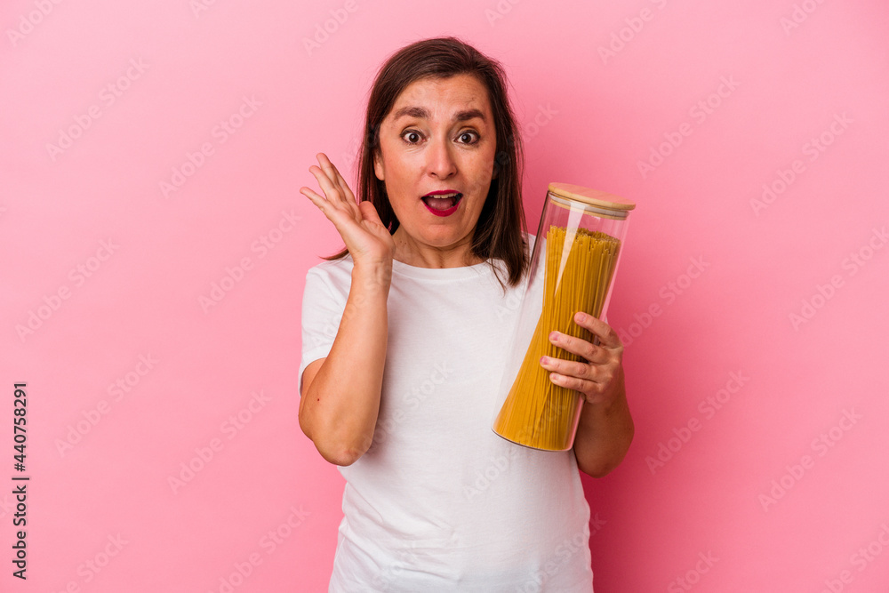 Middle age caucasian woman holding a pasta jar isolated on pink background surprised and shocked. Middle age caucasian woman holding a pasta jar isolated on pink background surprised and shocked.