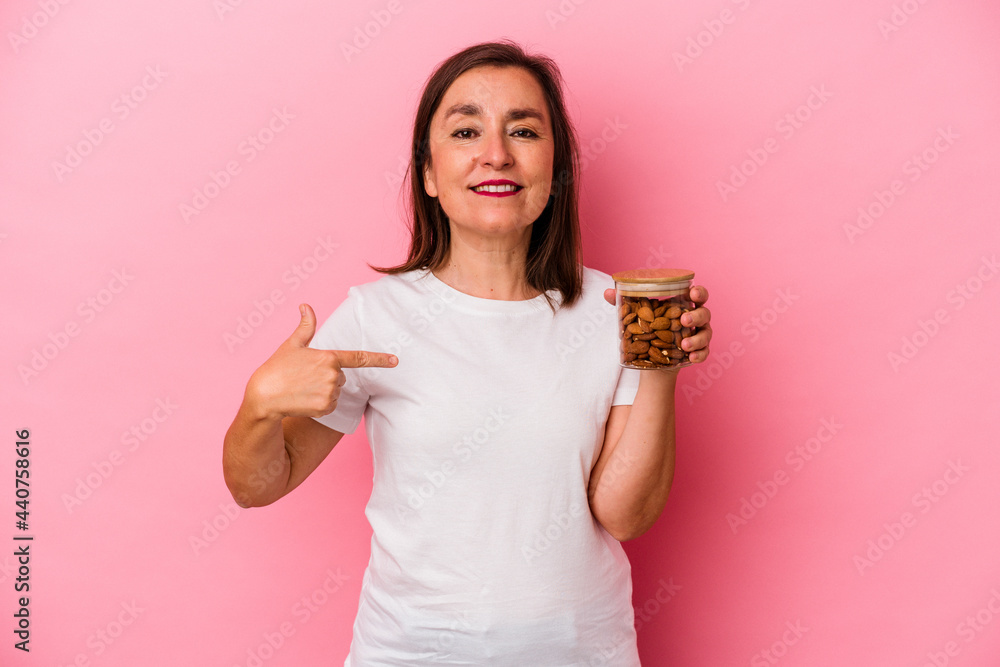 Middle age caucasian woman holding an almond jar isolated on pink background person pointing by hand to a shirt copy space, proud and confident Middle age caucasian woman holding an almond jar isolated on pink background person pointing by hand to a shirt copy space, proud and confident
