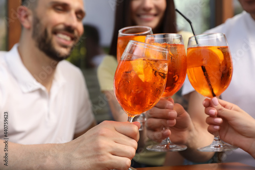 Friends clinking glasses of Aperol spritz cocktails outdoors, closeup