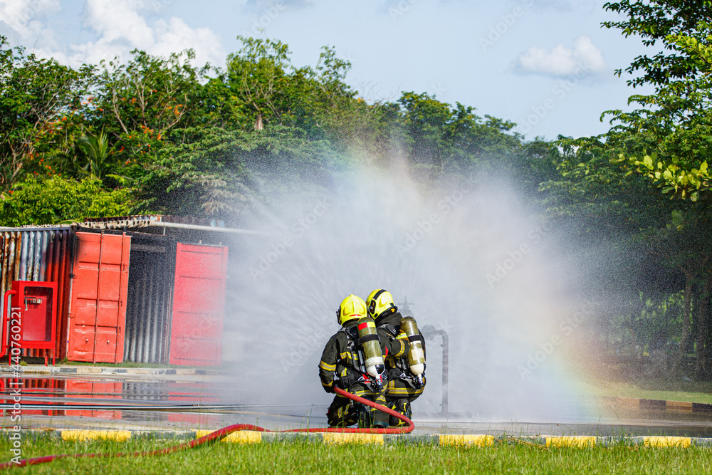 Fototapeta premium Two firefighter water spray by high pressure nozzle in fire fighting operation. Fire and rescue training school regularly to get ready.
