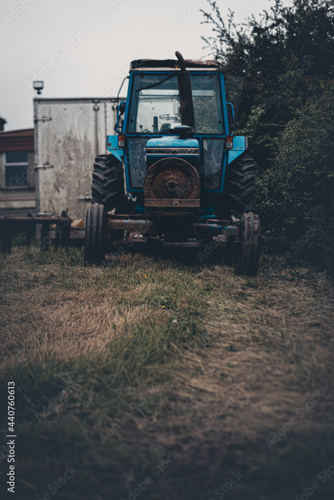 An abandoned old blue tractor stored in a field in the UK with overcast skies An abandoned old blue tractor stored in a field in the UK with overcast skies