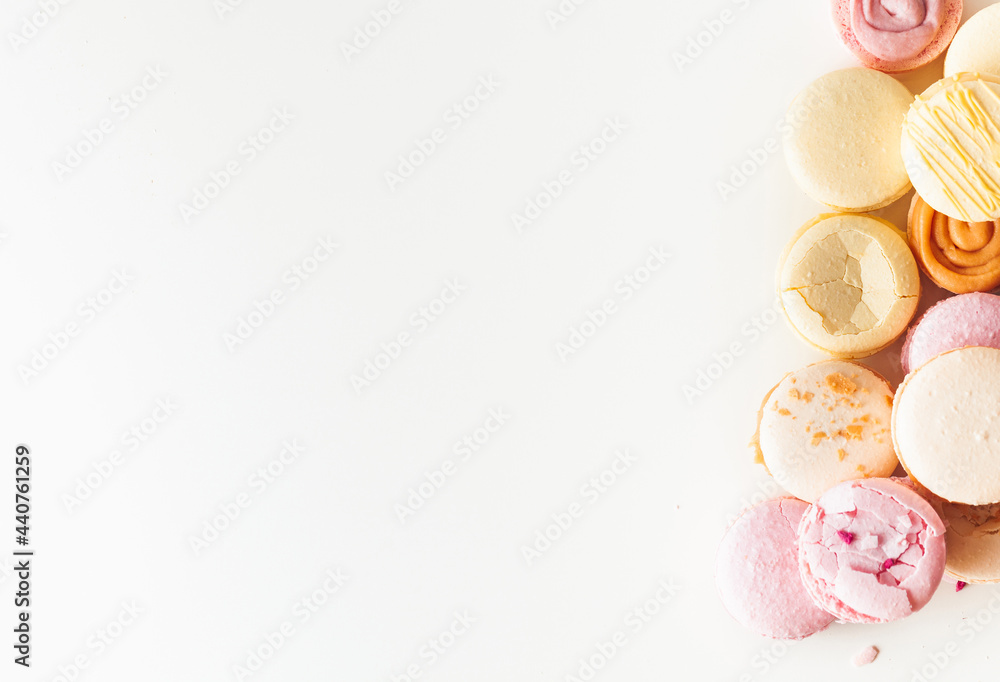 Flat lay of yellow and pink macaroons on the white background with a free space for text. Macro shot of cracked French sweet dessert cookies with crumbs Flat lay of yellow and pink macaroons on the white background with a free space for text. Macro shot of cracked French sweet dessert cookies with crumbs