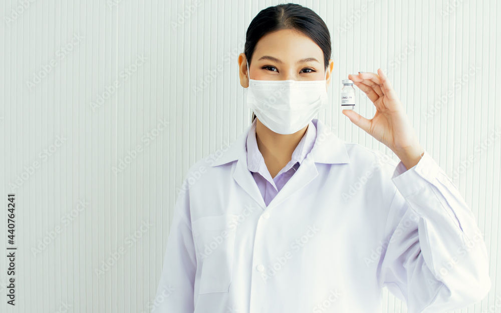 Female smart Asian professional doctor wearing face mask, white gown uniform, researching, holding and showing medical vaccine liquid vial for injection to patients protect virus with copy space. Female smart Asian professional doctor wearing face mask, white gown uniform, researching, holding and showing medical vaccine liquid vial for injection to patients protect virus with copy space.