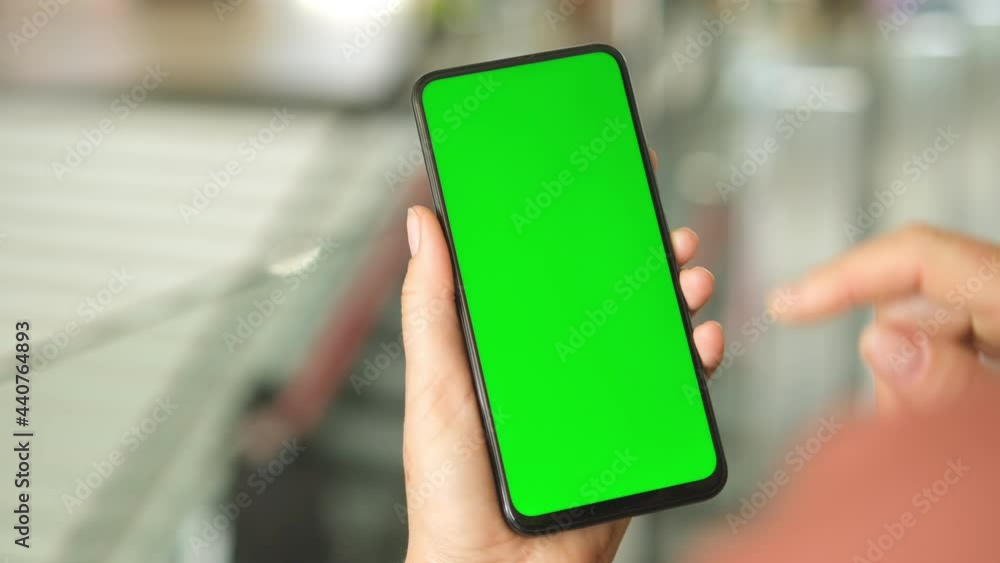 Mall. Shopping center. Back view of brunette holding chroma key green screen smartphone watching content. Shopping online. Gadgets and contemporary people concept. Mall. Shopping center. Back view of brunette holding chroma key green screen smartphone watching content. Shopping online. Gadgets and contemporary people concept.