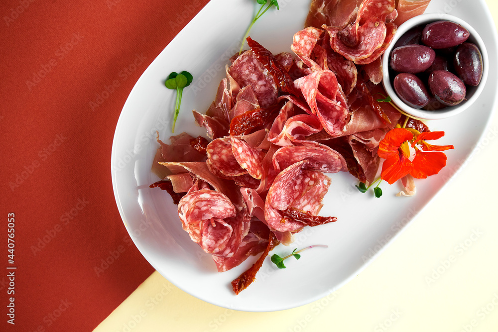 Appetizer - antipasti meat plate with salami, jamon and olives on bright colored backgrounds