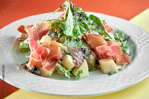 Delicious mix salad with jamon and pear in a white plate on bright colored backgrounds