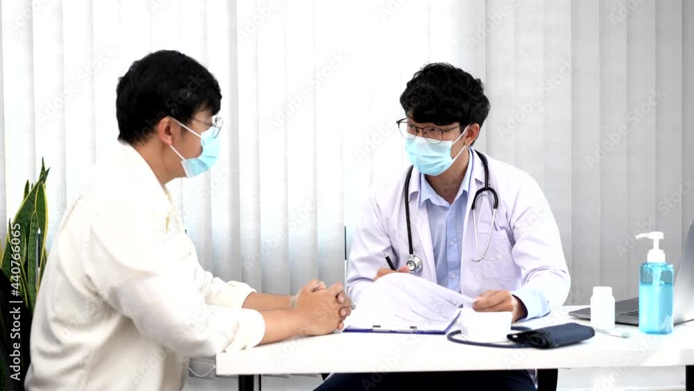 Medical concept a smart male doctor wearing a mask consulting with patient about how to recover from Coronavirus outbreak (COVID-19) at his modern clinic. Medical concept a smart male doctor wearing a mask consulting with patient about how to recover from Coronavirus outbreak (COVID-19) at his modern clinic.
