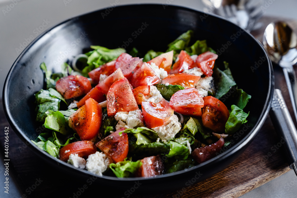 Salad with goat cheese, tomato, iceberg lettuce in big black bowl. Healthy eating, healthy lifestyle concept.