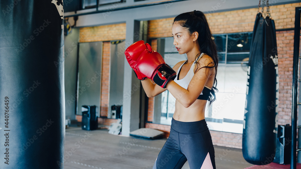 Young Asia lady kickboxing exercise workout punching bag tough female fighter practice boxing in gym fitness class. Sportswoman recreational activity, functional training, healthy lifestyle concept.