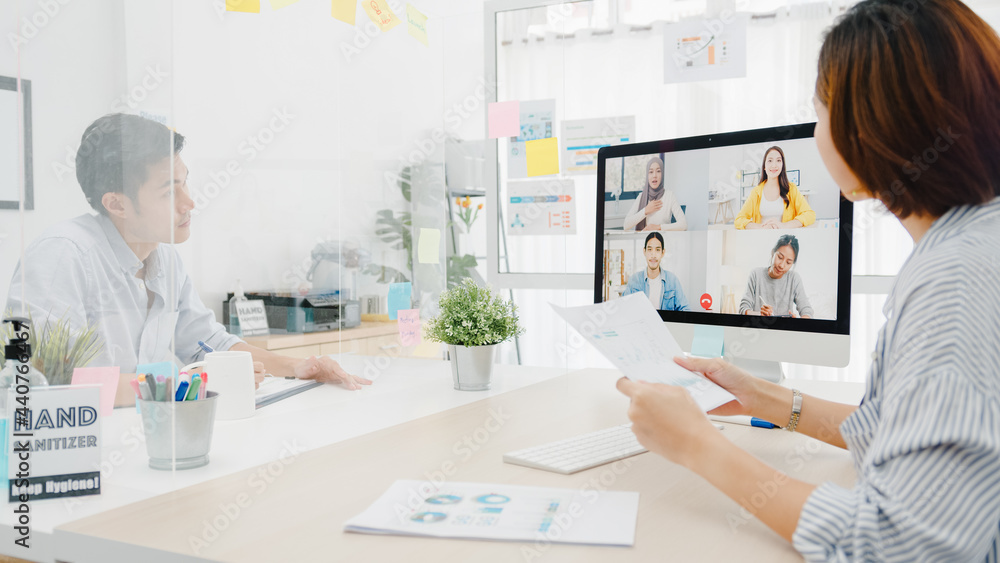 Obraz premium Asia businesspeople using desktop talk to colleagues discussing business brainstorm about plan in video call meeting in new normal office. Lifestyle social distancing and work after corona virus.