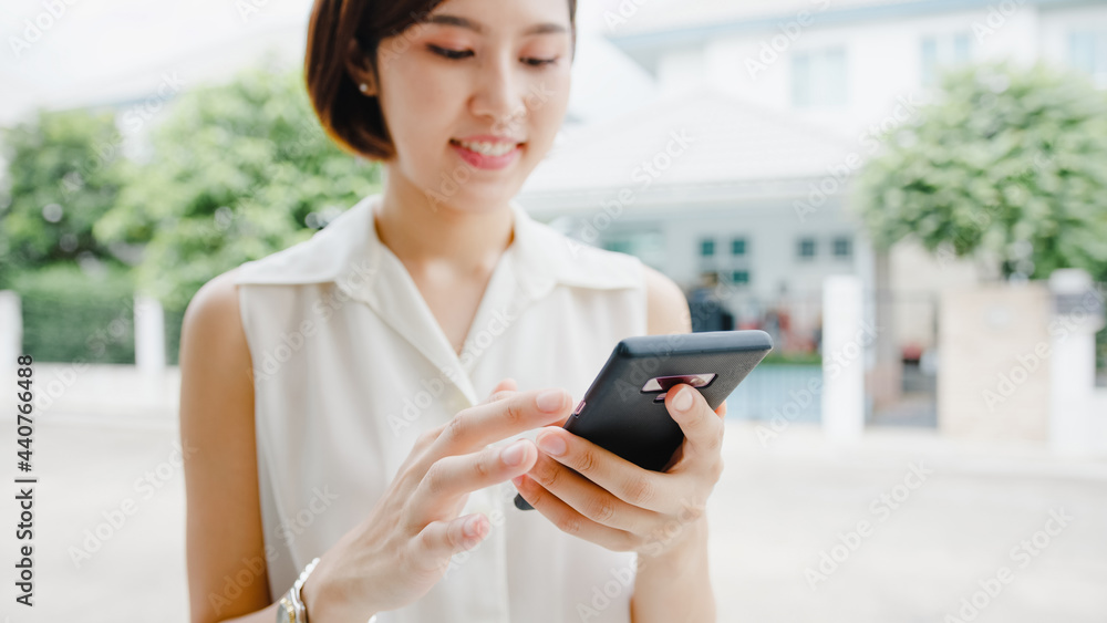 Attractive young Asia businesswoman using mobile phone checking social media internet, chatting with friends outside on street in city. Lifestyle new normal after coronavirus and social distancing.
