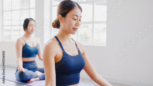 Young Asian sporty attractive people practicing yoga lesson with instructor. Asia group of women exercising healthy lifestyle in fitness studio. Sport activity, gymnastics or ballet dancing class. © tirachard