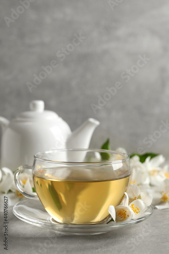 Glass cup of jasmine tea and fresh flowers on grey table