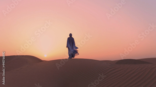 Portrait of beautiful Arab woman weared in blue traditional dress in the desert during sunset.