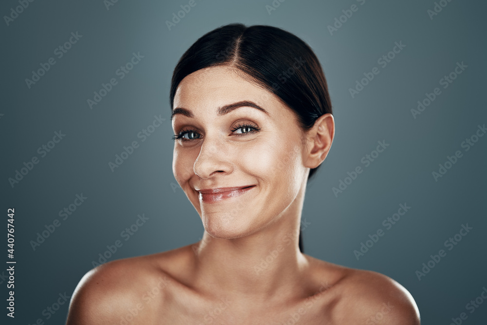 Beautiful young woman making a face and smiling while standing against grey background Beautiful young woman making a face and smiling while standing against grey background
