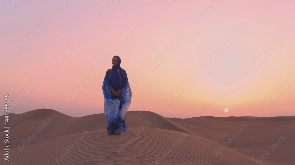 Portrait of beautiful Arab woman weared in blue traditional dress in the desert during sunset.