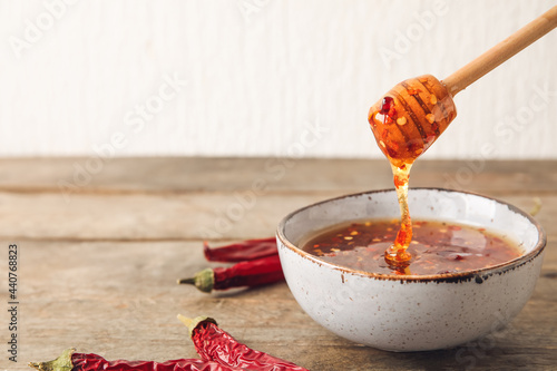 Pouring of hot honey from dipper into bowl on wooden table photo