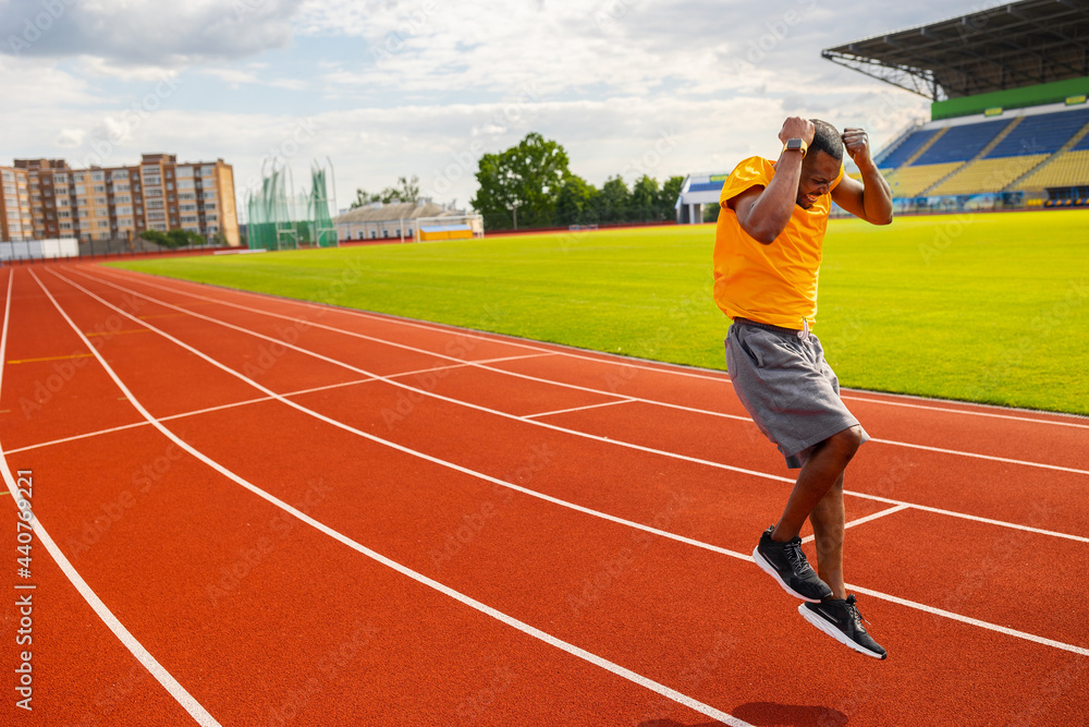 Obraz premium Joyful Afro American runner in yellow sportswear happily jumping and winning the runner competition, receiving first place, training and working hard to win the race. Victory concept