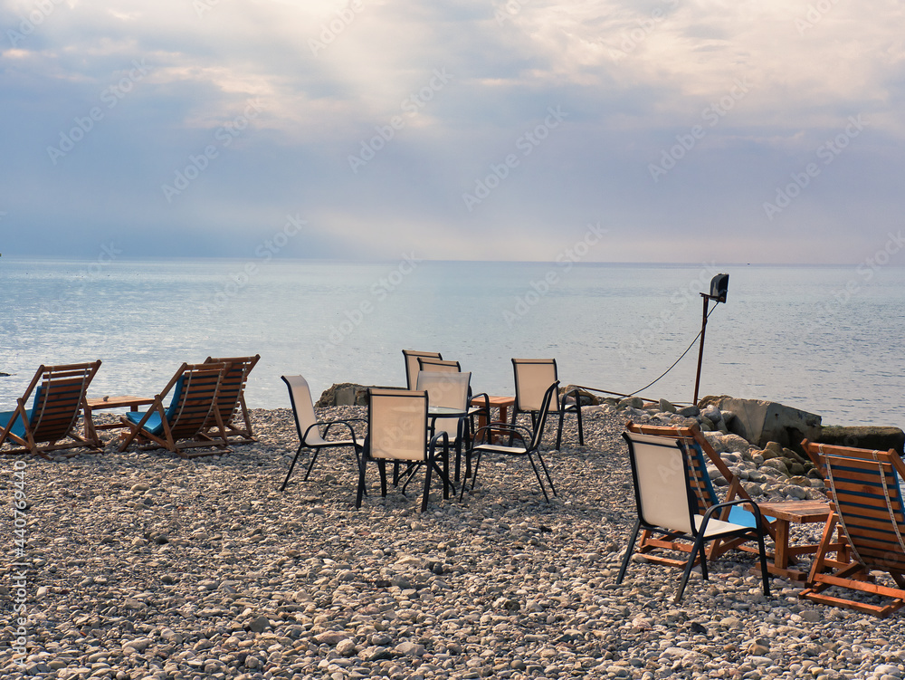 Chairs and tables of a bar on a stone beach with cloudy sky