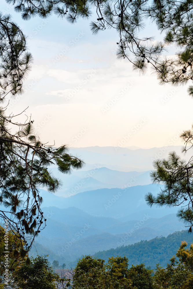 Beautiful mountain layers with blue sky background, and pine leafs frame around the image.