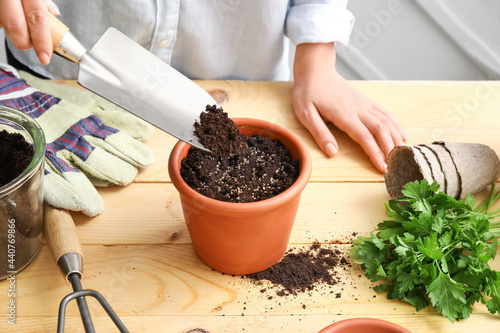 Woman filling pot with soil on wooden table
