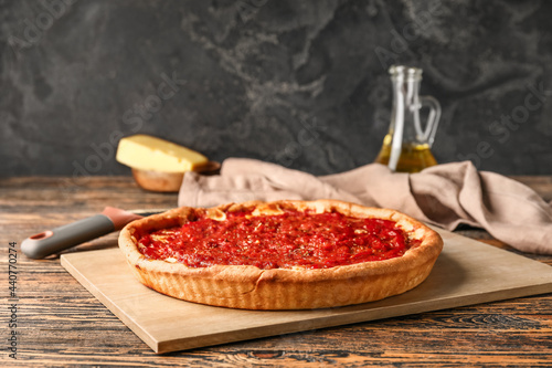 Board with tasty Chicago-style pizza on dark background