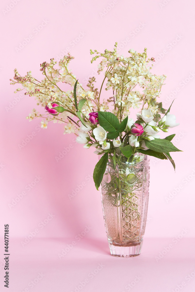 Bouquet of meadowsweet (Latin Filipndula), jasmine and wild roses in a vase on a pink background.
