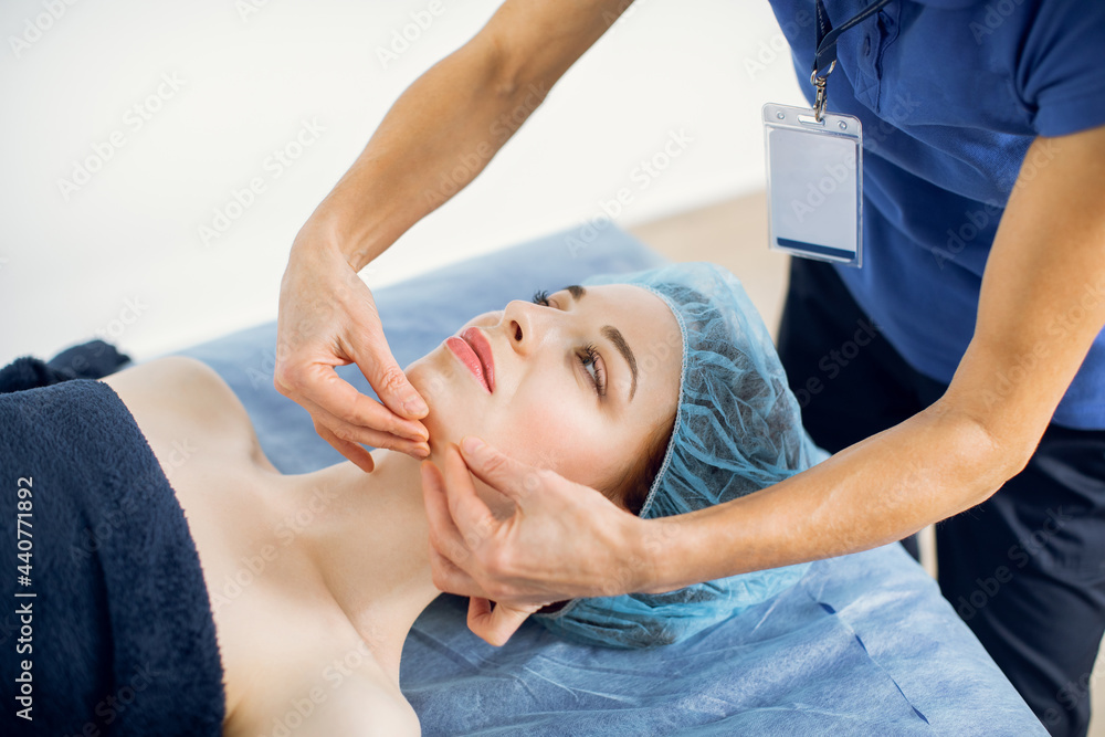 Pretty young european woman having facial massage for her skin on a face in modern beauty salon. Close up of hands of female masseur doing face lifting massage for female client.