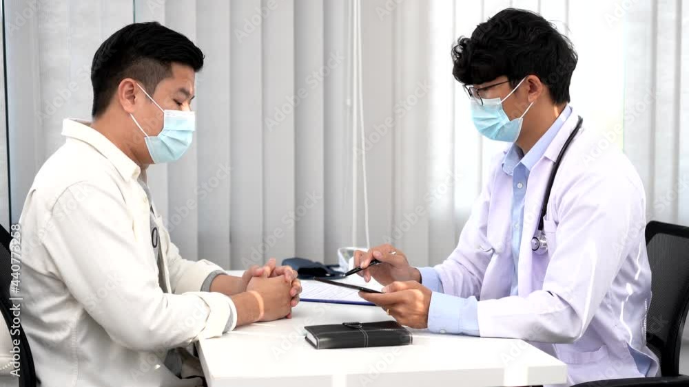 Medical concept a smart male doctor wearing a mask consulting with patient about how to recover from Coronavirus outbreak (COVID-19) at his modern clinic. Medical concept a smart male doctor wearing a mask consulting with patient about how to recover from Coronavirus outbreak (COVID-19) at his modern clinic.