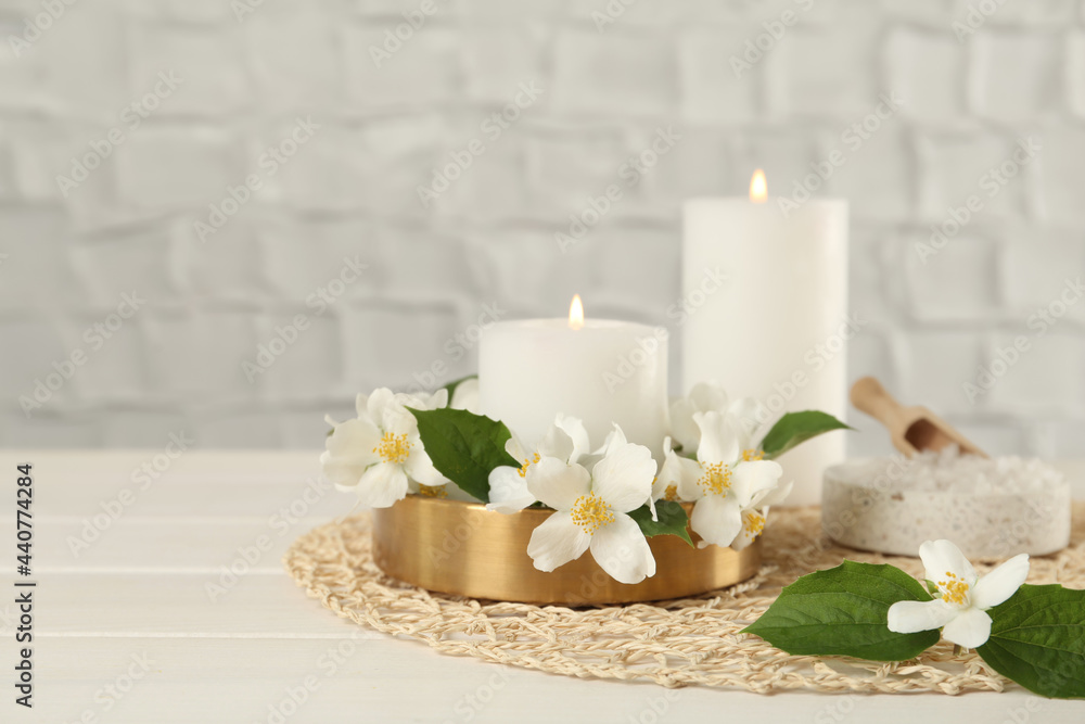 Beautiful jasmine flowers and burning candles on white wooden table, space for text