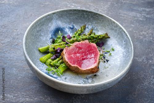 Modern style traditional green asparagus with fried dry aged sliced beef fillet steak and green asparagus served as close-up on a Nordic design plate