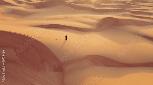 Aerial view from a drone flying next to a woman in abaya United Arab Emirates traditional dress walking on the dunes in the desert of the Empty Quarter. Abu Dhabi, UAE.