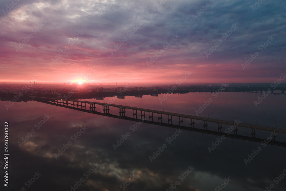 Aerial drone filmed sunset, burning sky over the city and water, beautiful sunset or sunrise. Panoramic view over the bridge with the sun