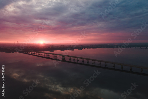 Aerial drone filmed sunset, burning sky over the city and water, beautiful sunset or sunrise. Panoramic view over the bridge with the sun