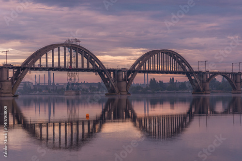 Fototapeta Naklejka Na Ścianę i Meble -  Bridge over the water during beautiful sunset and sunrise sun. Sunset over the bridge, purple blue yellow orange sky.