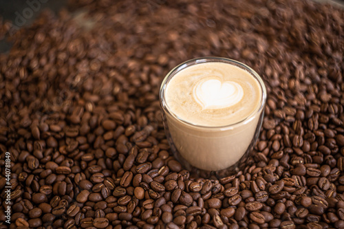 Coffee. Glass cup with cappuccino with latte art stands on coffee beans. 