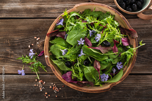 Asian salad mix with baby spinach, mizuna salad, edible flowers and olives on wooden background, top view